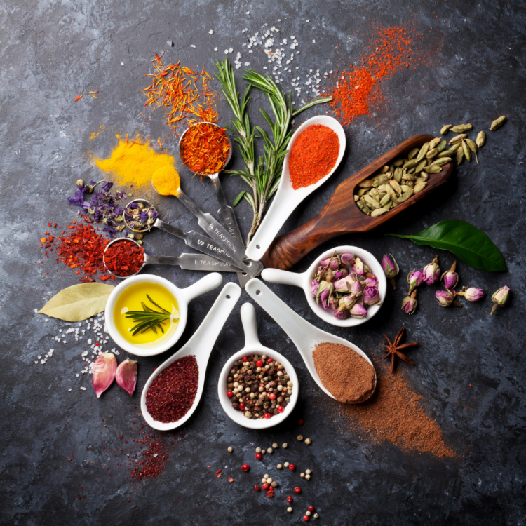 Measuring spoons filled with various spices are arranged in a circle on a slate table.
